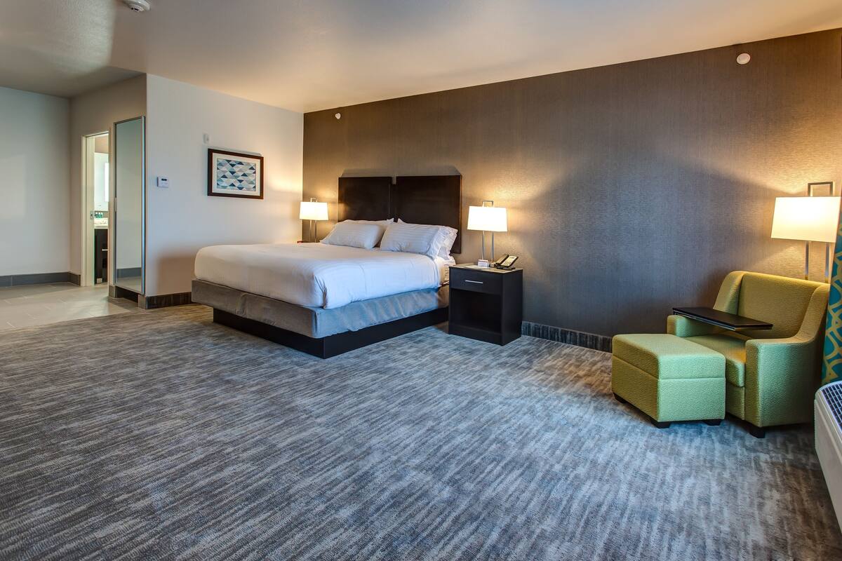 A hotel room with a bed, bedside tables, a chair, and a carpeted floor.