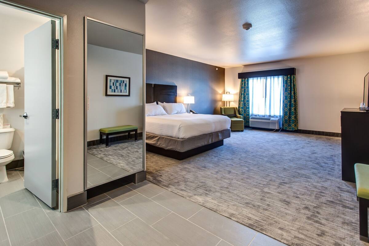 A hotel room with a bed, bedside table, lamp, and a view of the outside through a window.