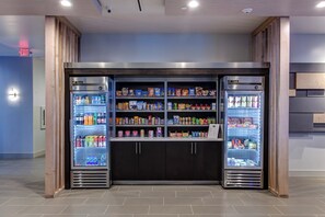 Una estación de autoservicio para bebidas con múltiples dispensadores refrigerados y estantes con bocadillos.