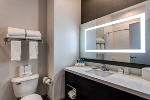 Een moderne badkamer met een witte wastafel, een grote spiegel met ingebouwde verlichting en een toilet. Handdoeken en toiletartikelen liggen op de wastafel.