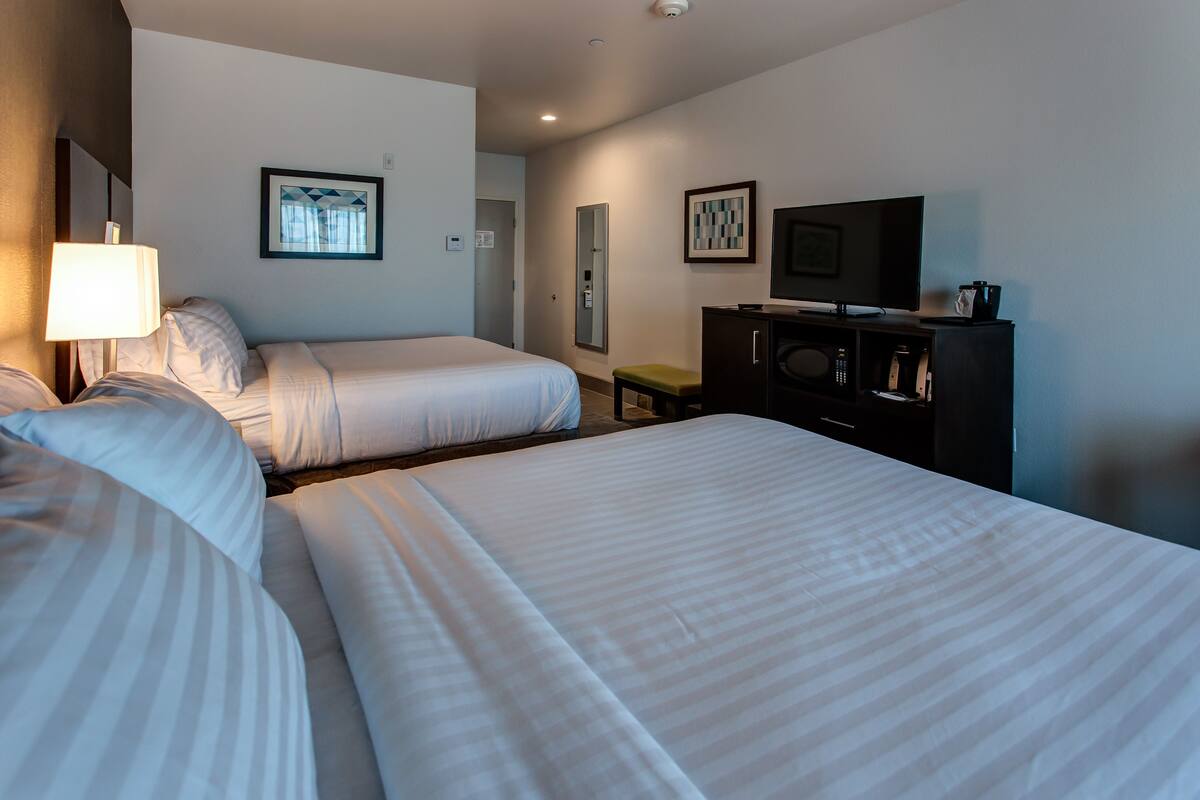 A hotel room with two beds, a desk with a television, a mirror, and a small stool.