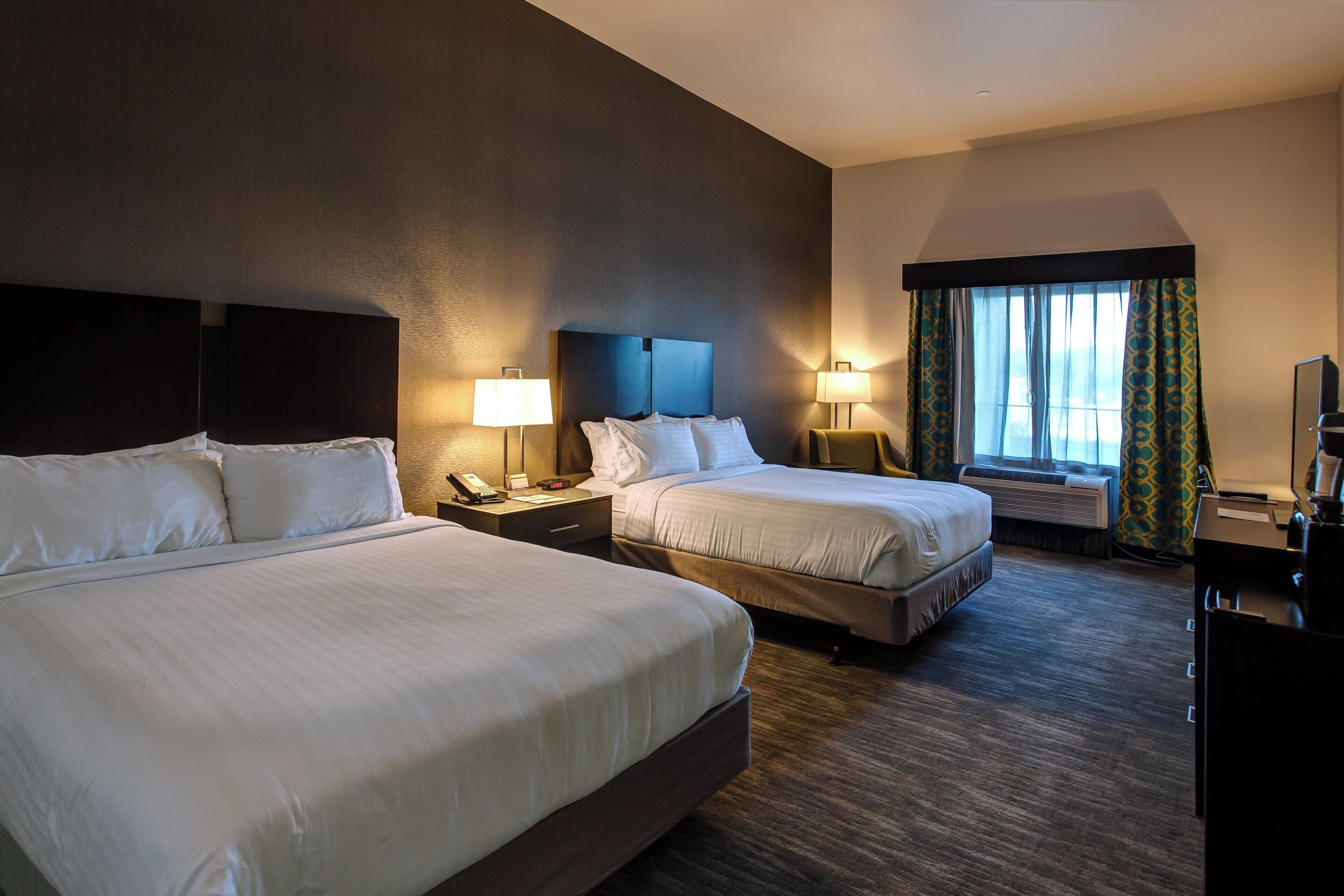 A hotel room with two beds, bedside lamps, a desk, and a television.
