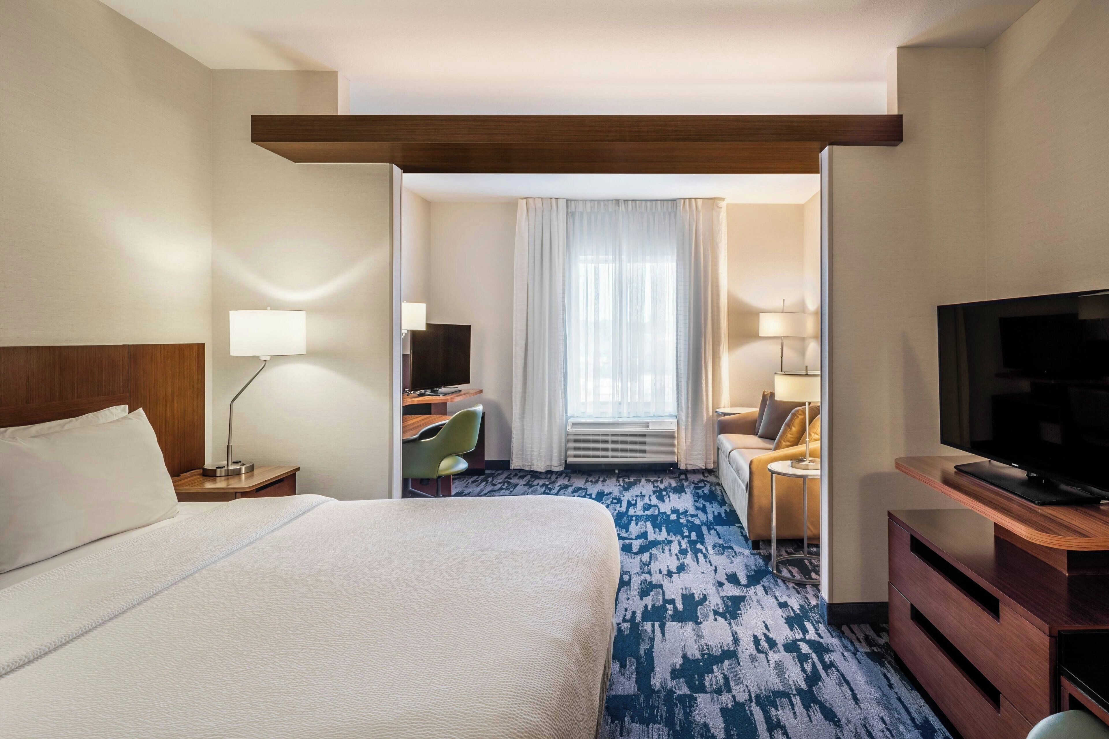 A hotel room with a large bed, a desk with a chair, a television, and a sofa.
