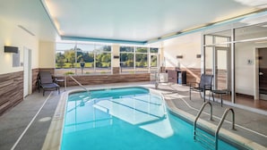 Ein überdachter Swimmingpool mit Glaswänden, Blick auf Grünflächen und einem modernen Interieur mit hoher Decke und Sitzbereichen.