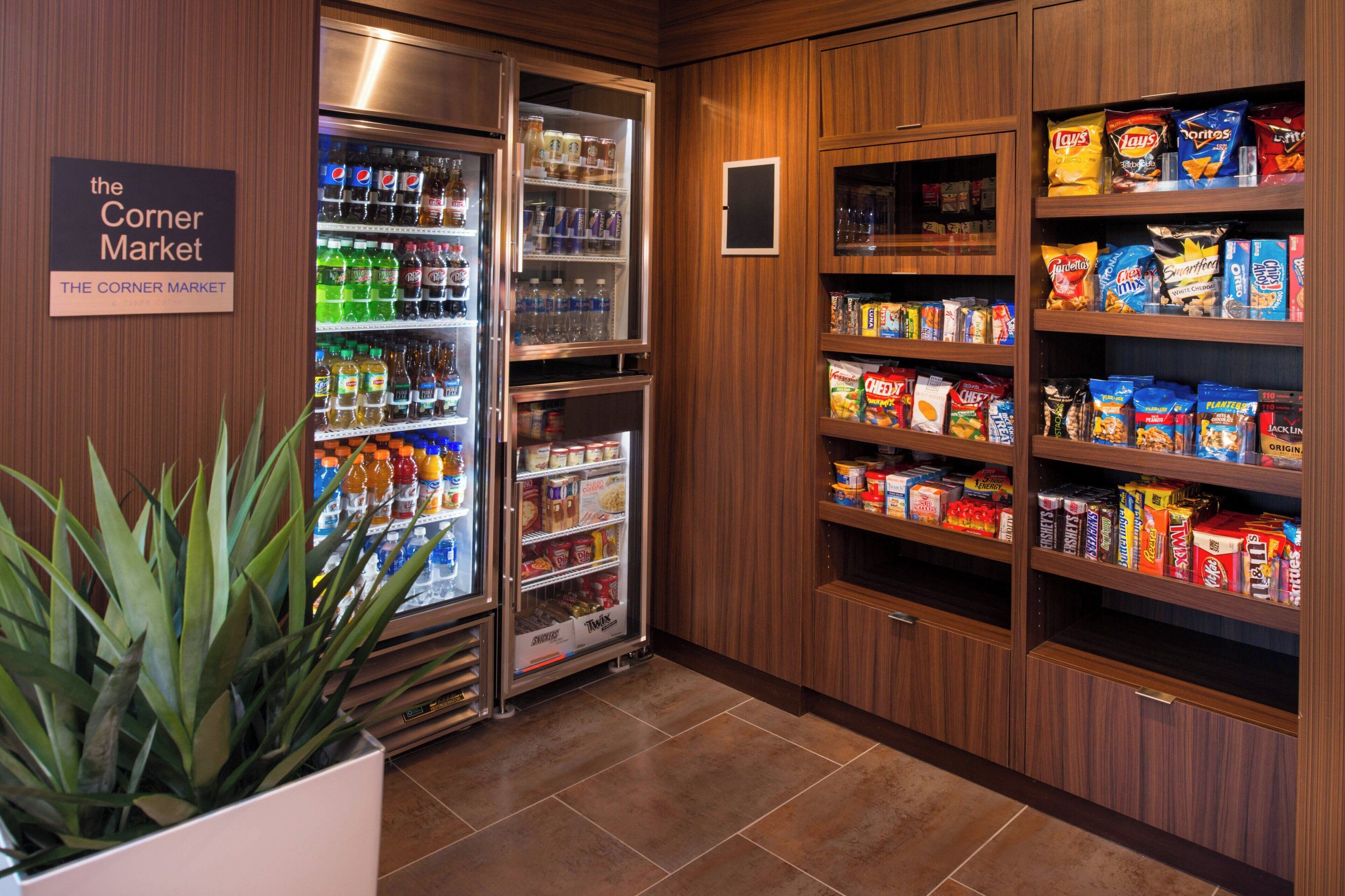 A corner market with refrigerated and non-refrigerated shelves stocked with beverages, snacks, and packaged goods.