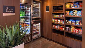A corner market with refrigerated and non-refrigerated shelves stocked with beverages, snacks, and packaged goods.