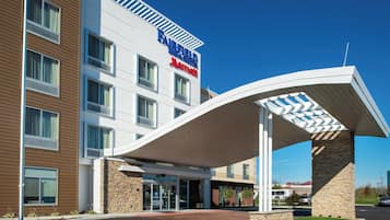 Um hotel Fairfield Inn & Suites com design moderno, apresentando uma entrada coberta e um céu azul límpido.