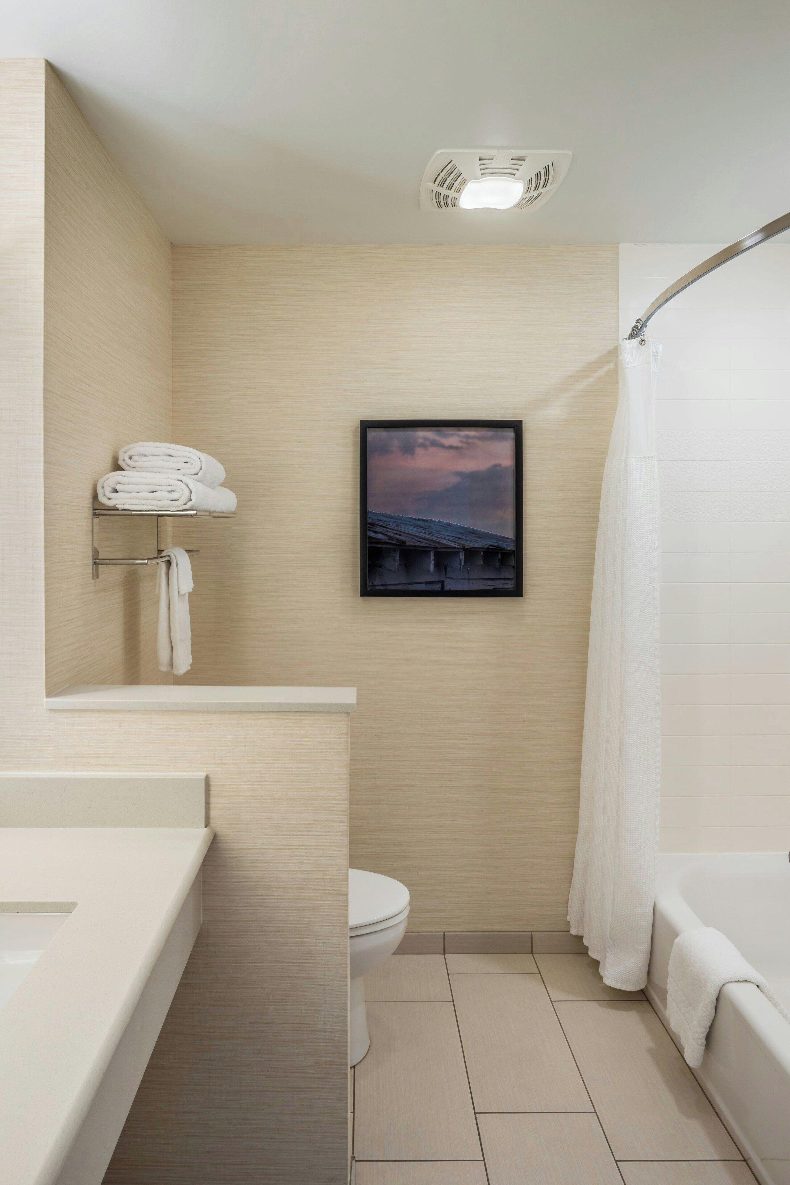 Une salle de bain comprenant des toilettes, un lavabo, une baignoire, un porte-serviettes et un tableau encadré au mur.