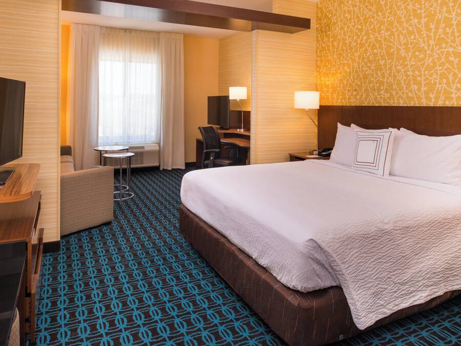 A hotel room with a large bed, a desk with a chair, a TV, and a small table.