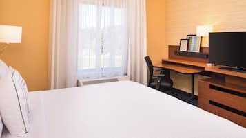 Una habitación de hotel con una cama grande, un escritorio con una silla, un televisor y una ventana con cortinas.