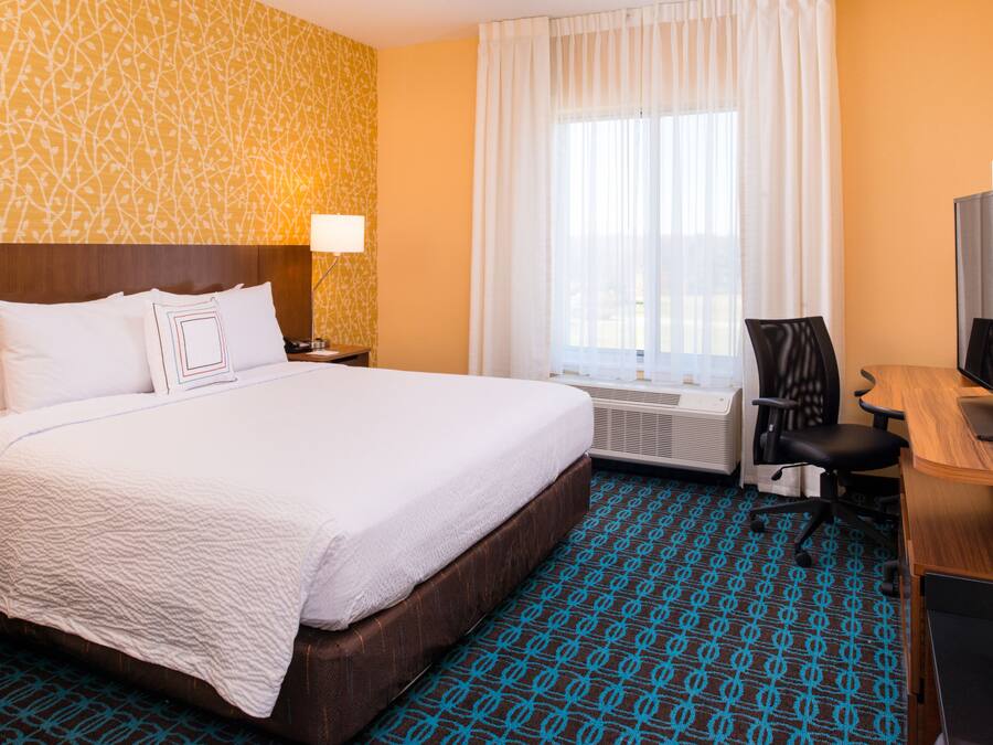 Habitación de hotel con una cama grande, un escritorio, una silla, un televisor y una ventana con cortinas.