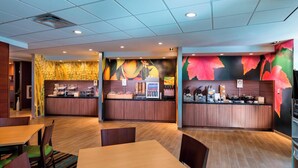 A modern restaurant with wooden flooring, a counter with food items, and a seating area with tables and chairs. - Fairfield Inn & Suites by Marriott Dallas Waxahachie (Waxahachie)