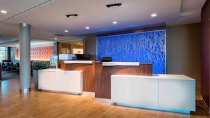 A modern reception area with a reception desk, a blue abstract wall, and a seating area with chairs and tables. - Fairfield Inn & Suites by Marriott Dallas Waxahachie (Waxahachie)