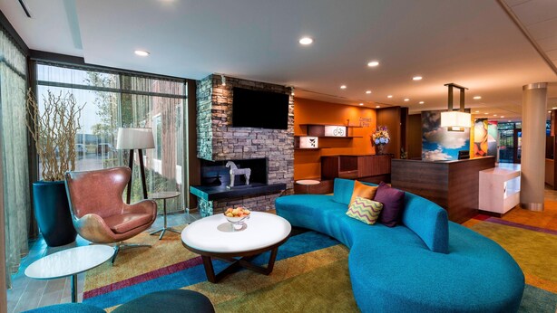 A modern living room with a stone fireplace, a blue sofa, a round coffee table, and a television mounted on the wall. - Fairfield Inn & Suites by Marriott Dallas Waxahachie (Waxahachie)