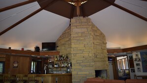 Zona de bar con chimenea de piedra, vigas de madera y una lámpara colgante.