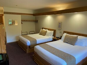 A hotel room with two beds, wooden headboards, a small bedside table with a phone, and a framed picture on the wall.