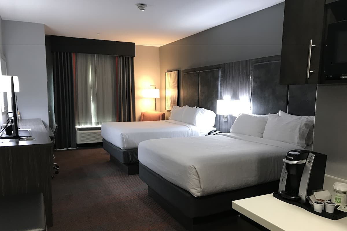 Une chambre d’hôtel avec deux lits, un bureau, une machine à café et une lampe.