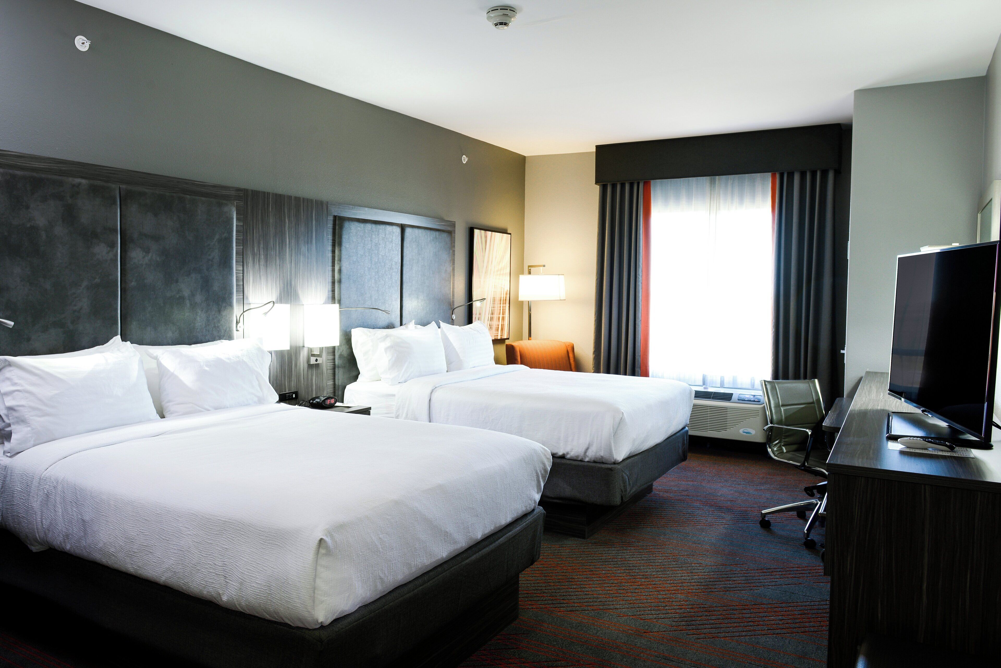 A hotel room with two beds, a desk with a television, and a window with curtains.