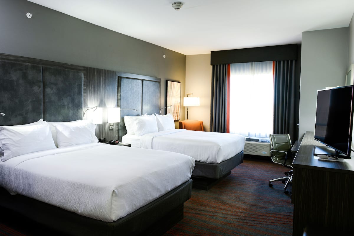 Une chambre d’hôtel avec deux lits, un bureau, une télévision et une fenêtre avec des rideaux.