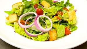 Une salade composée de laitue, de tomates, d’oignons rouges et de croûtons, servie dans une assiette blanche.