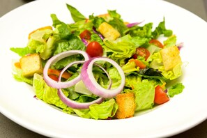 A salad with lettuce, tomatoes, red onions, and croutons on a white plate. - Holiday Inn Abilene - North College Area by IHG (Abilene)