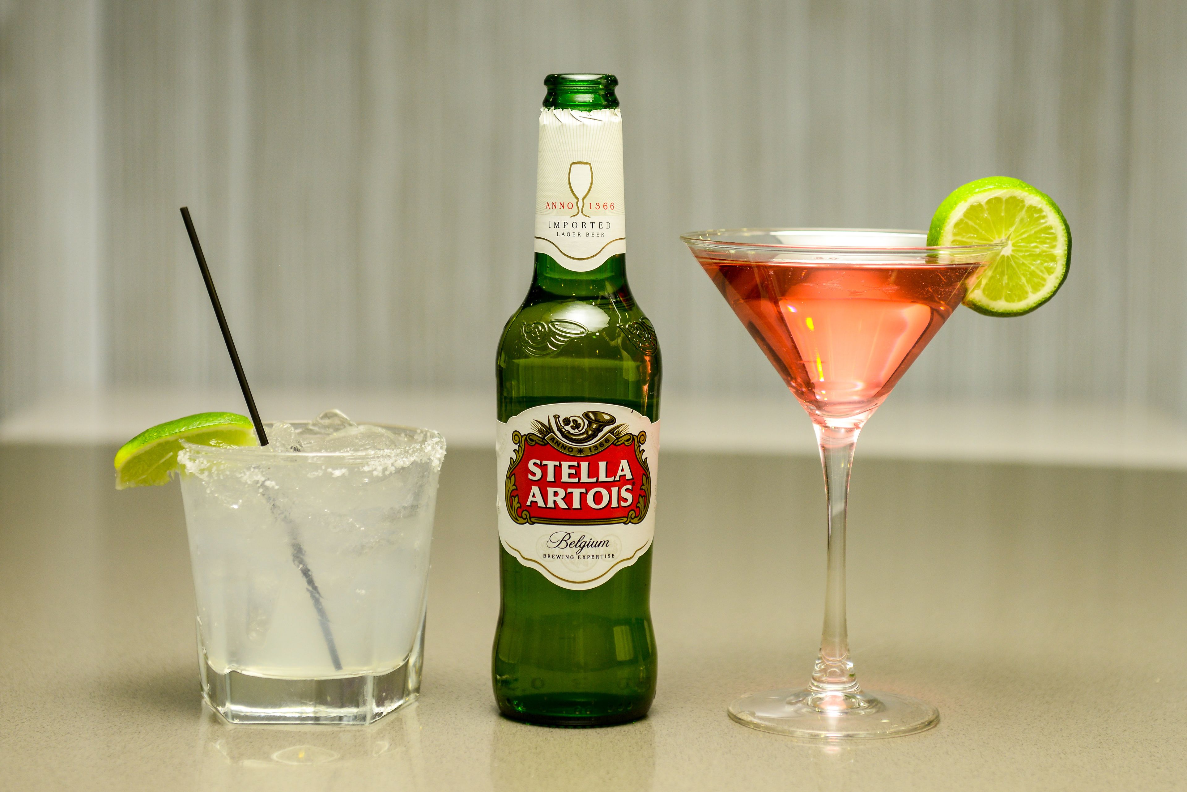 Een fles Stella Artois bier, een glas bier met een limoen en een roze cocktail met een limoen.