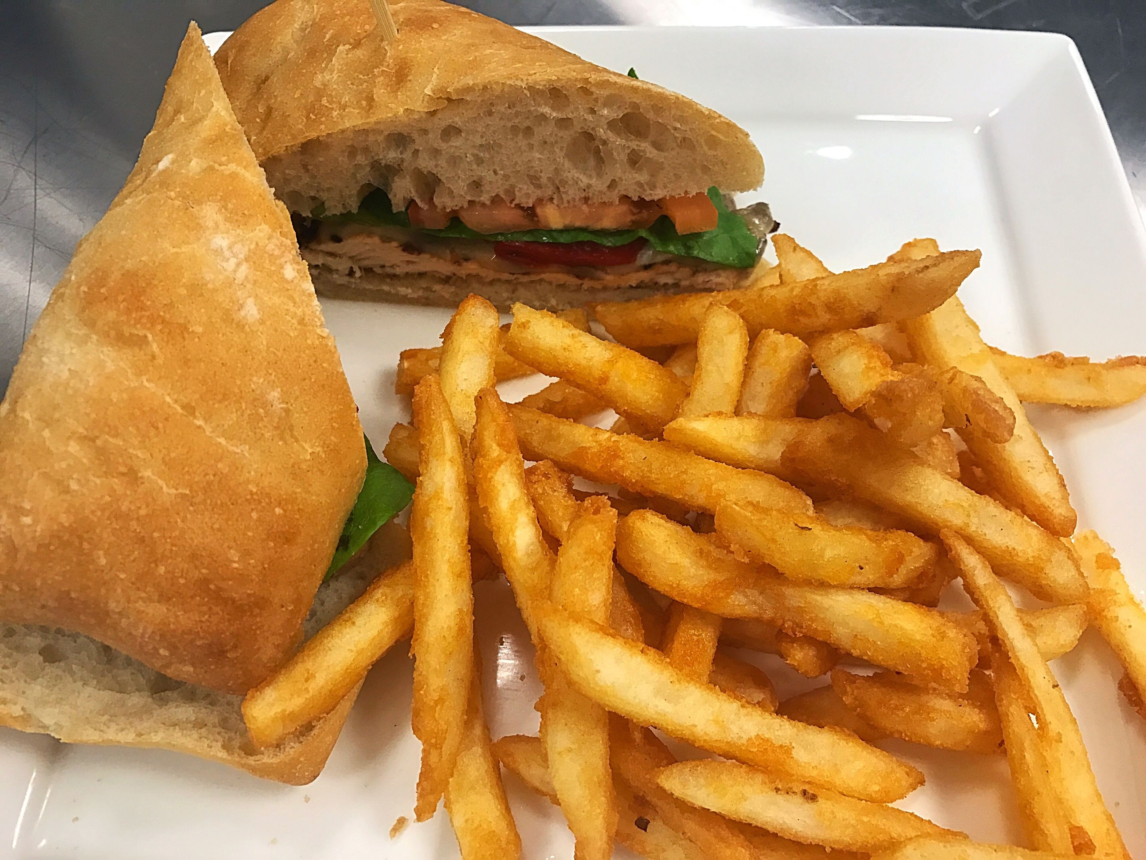 Un sándwich y una porción de papas fritas sobre un plato blanco.