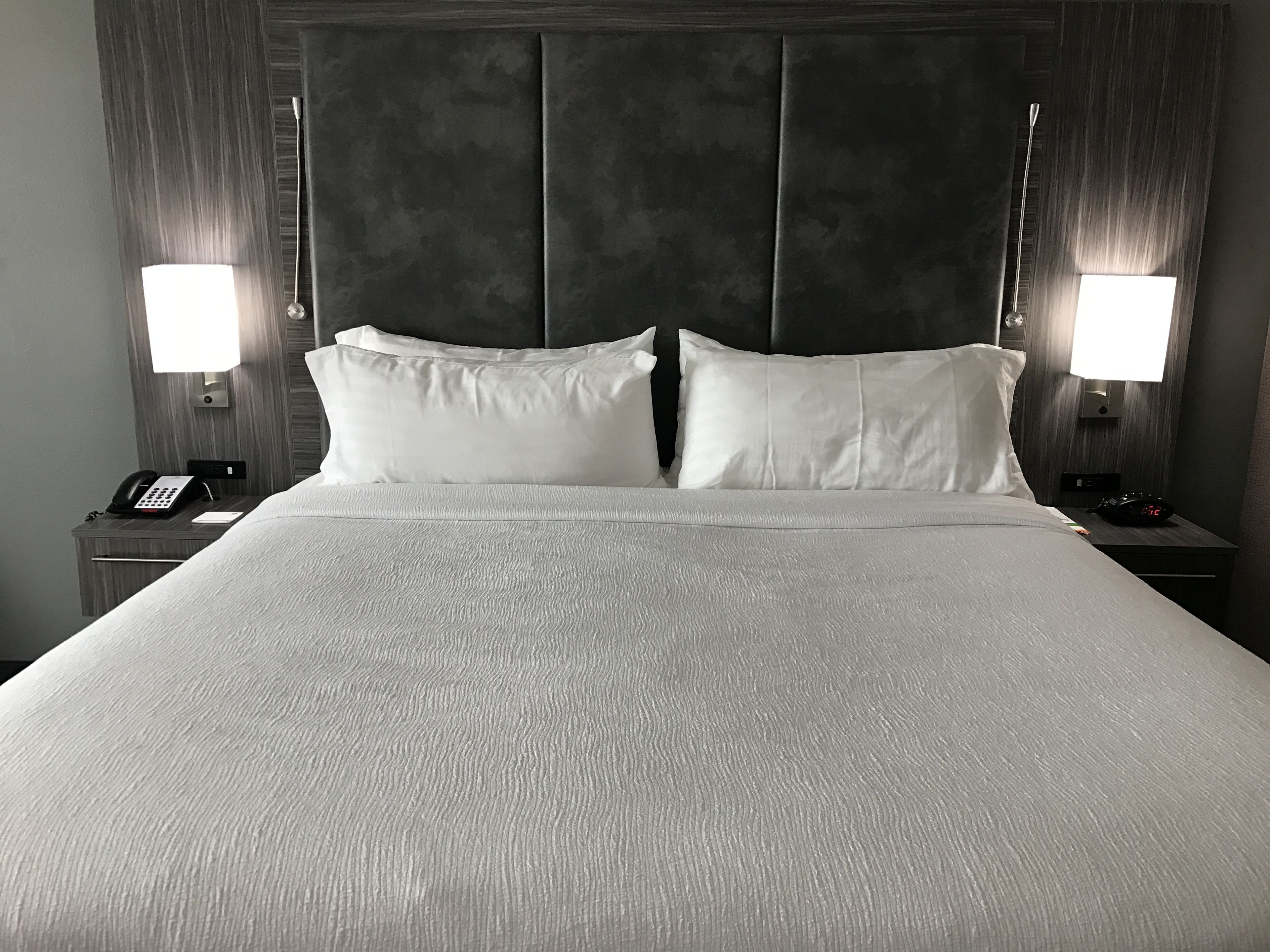 A neatly made bed with white linens, two bedside lamps, and a telephone on the nightstand.