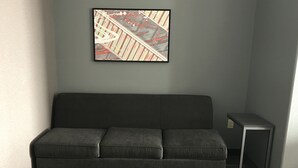 Een moderne kamer met een grijze bank, een klein tafeltje en een lijst met een afbeelding aan de muur.