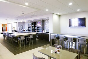 A modern hotel lobby with a bar area, seating, and a television screen.