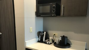 Een kitchenette voorzien van een magnetron, koffiezetapparaat en kleine koelkast.