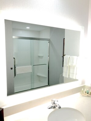 A bathroom with a large mirror, a glass-enclosed shower, and a white sink. - Holiday Inn Abilene - North College Area by IHG (Abilene)