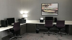 Een moderne kantoorruimte met twee bureaus, twee stoelen, een printer en een groot abstract schilderij aan de muur.