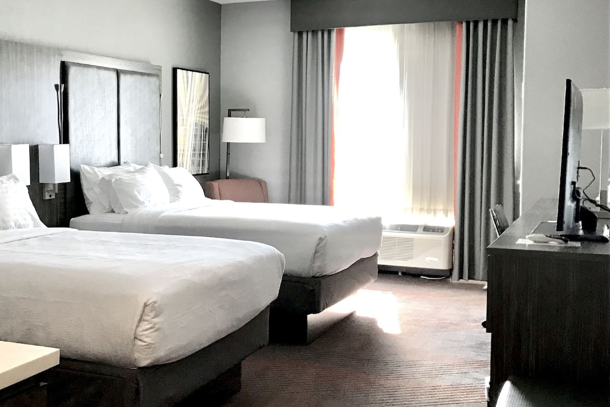 Une chambre d’hôtel avec deux lits, un bureau, une chaise, une télévision et une fenêtre avec des rideaux.