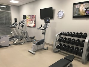 A gym with treadmills, an elliptical, a bench, and a rack of dumbbells.