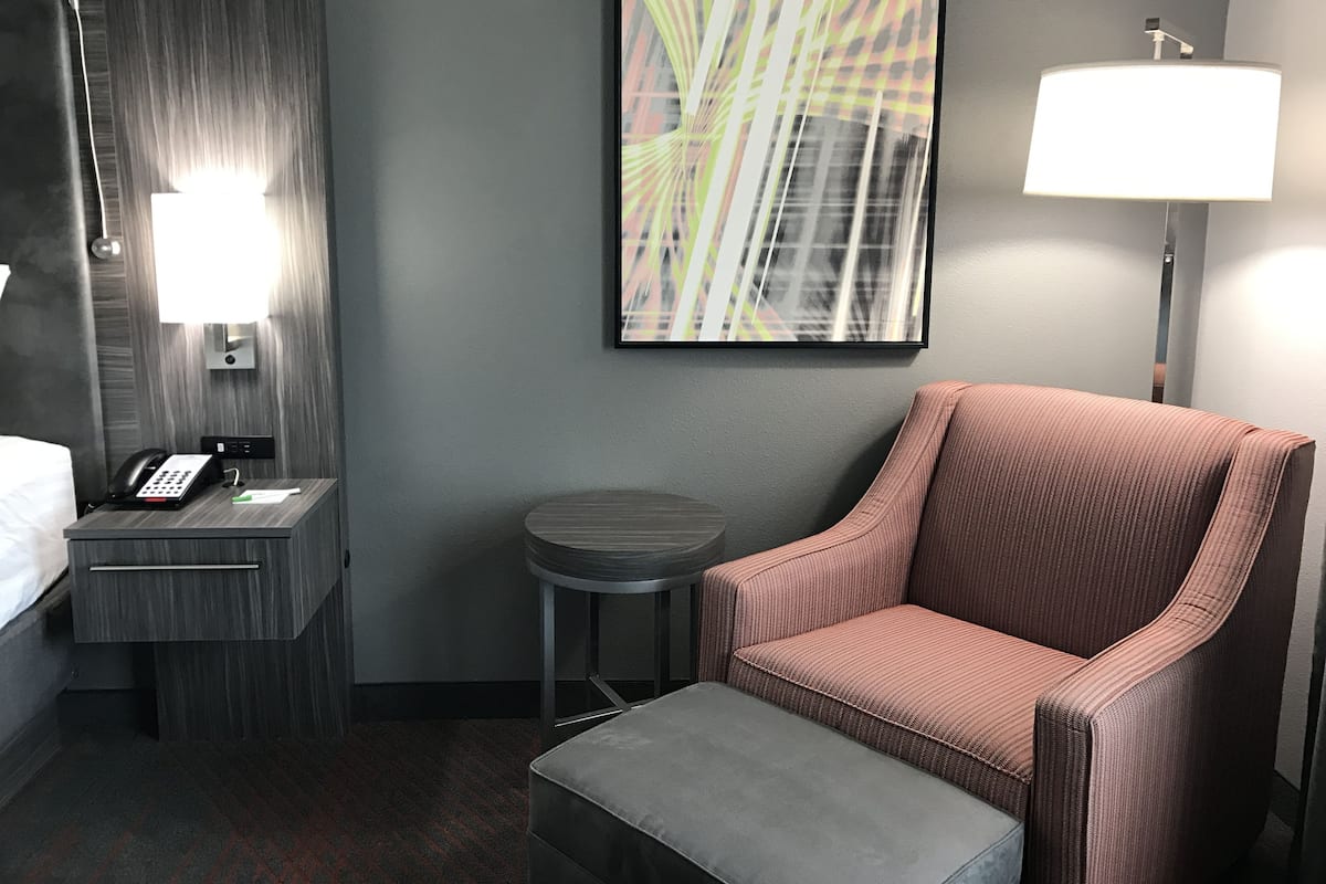 Une chambre d’hôtel avec un lit, un bureau avec un téléphone, une chaise, une petite table, une lampe et un tableau au mur.