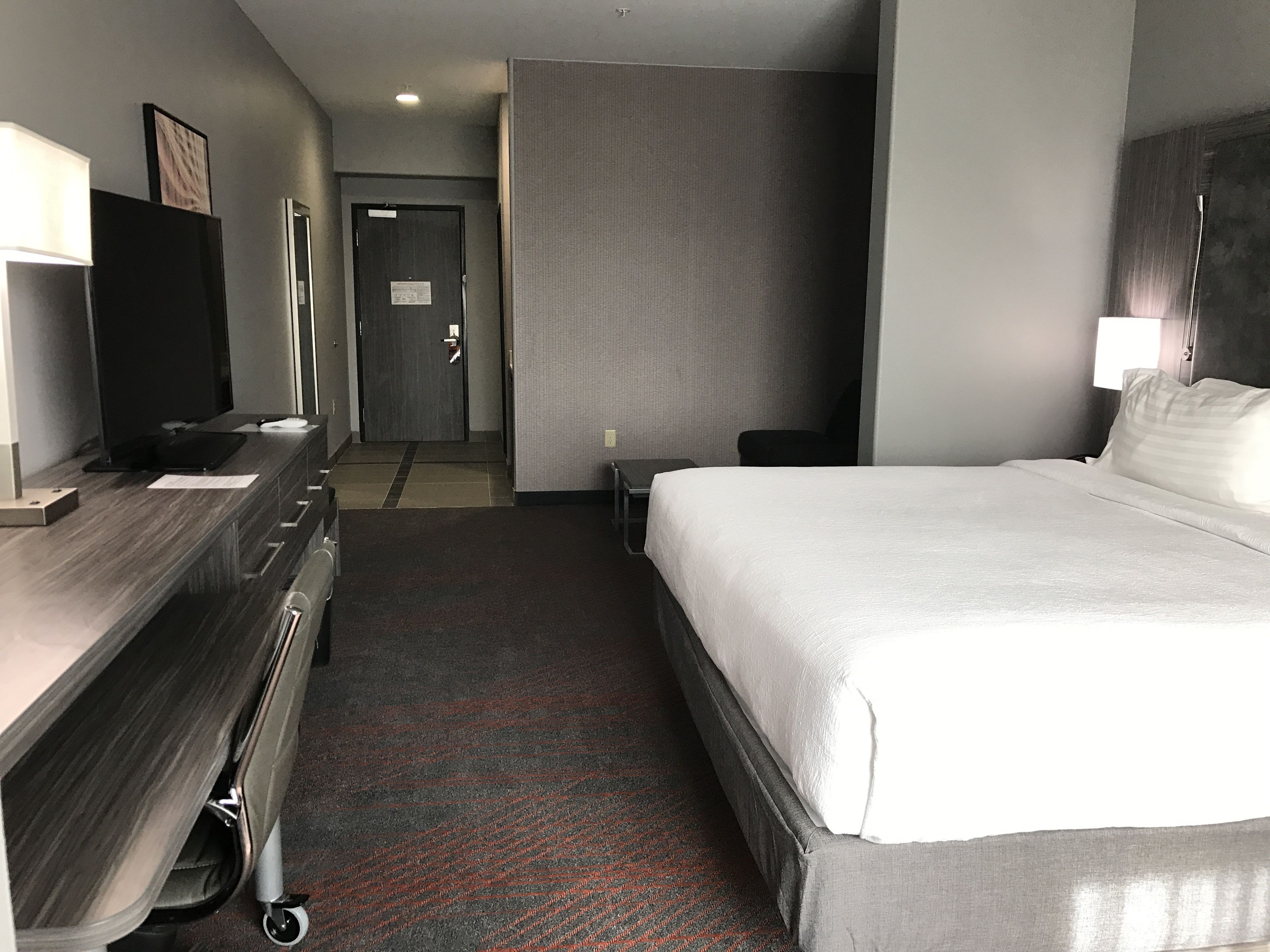 A hotel room with a bed, a desk with a computer, a chair, and a television.