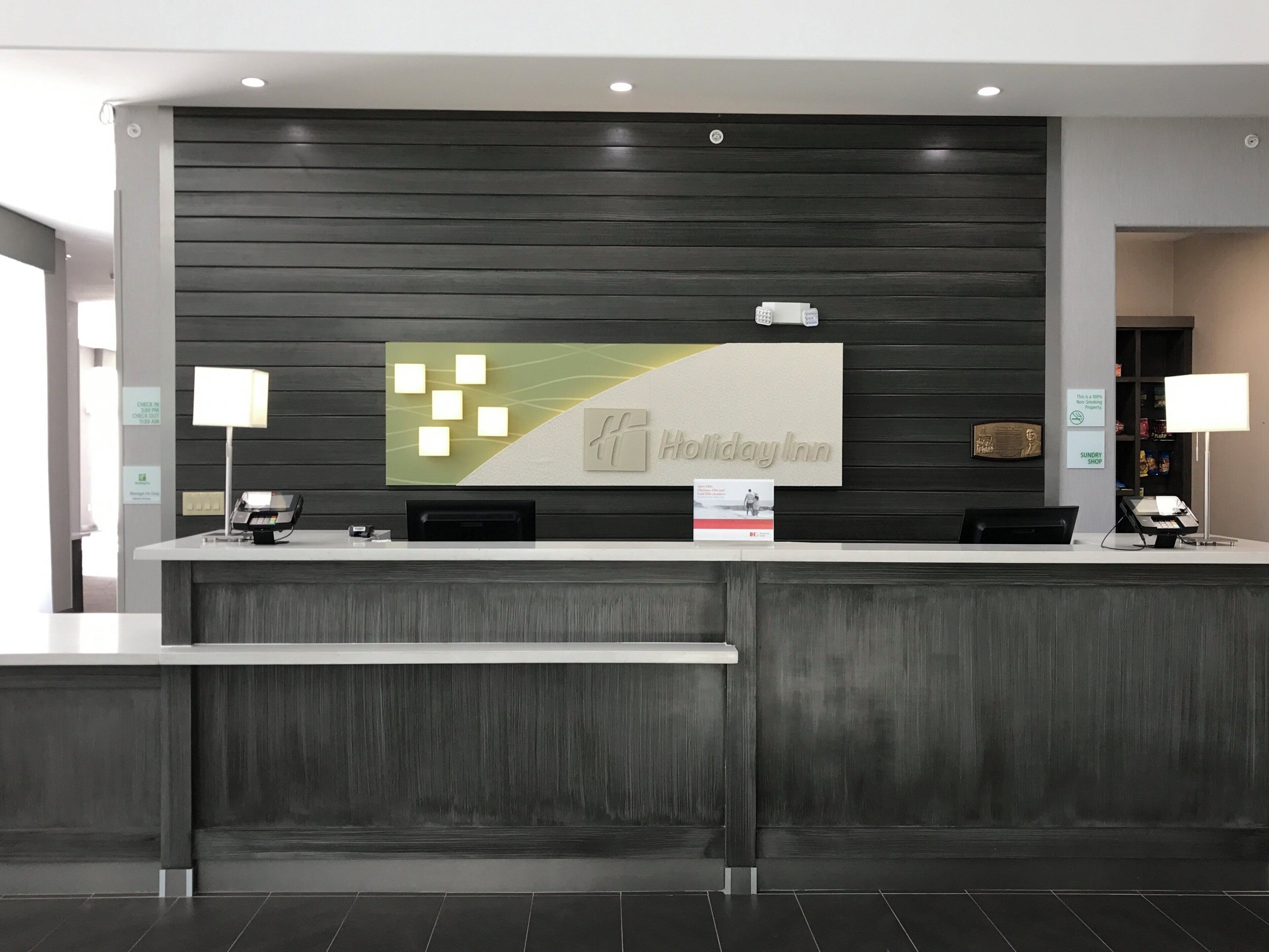Una recepción con el letrero de Holiday Inn, un mostrador de registro y un letrero de Sunday Shop.