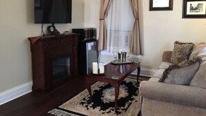 A living room with a fireplace, a television mounted on the wall, a sofa, and a coffee table. - Elmwood House (Eureka Springs)