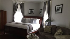 A hotel room with a large bed, a wooden headboard, a marble side table, a sofa, and a chandelier. - Elmwood House (Eureka Springs)