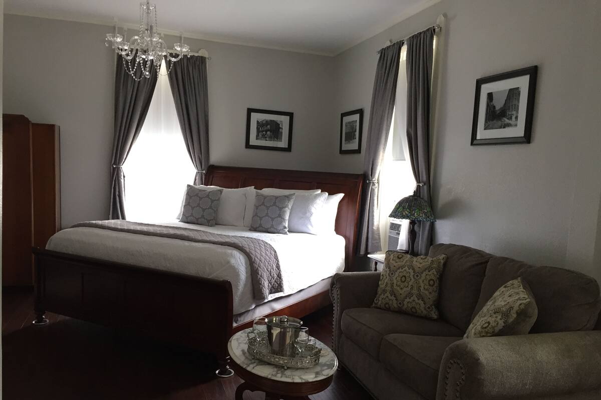 A hotel room with a large bed, a wooden headboard, a marble side table, a sofa, and a chandelier.