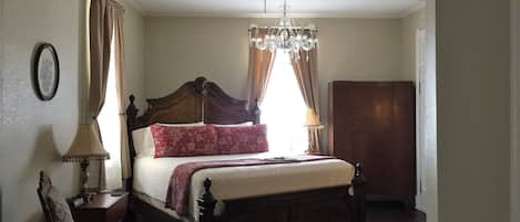 Une chambre à coucher avec un grand lit, une armoire en bois, une chaise, une table de chevet avec une lampe et un lustre.