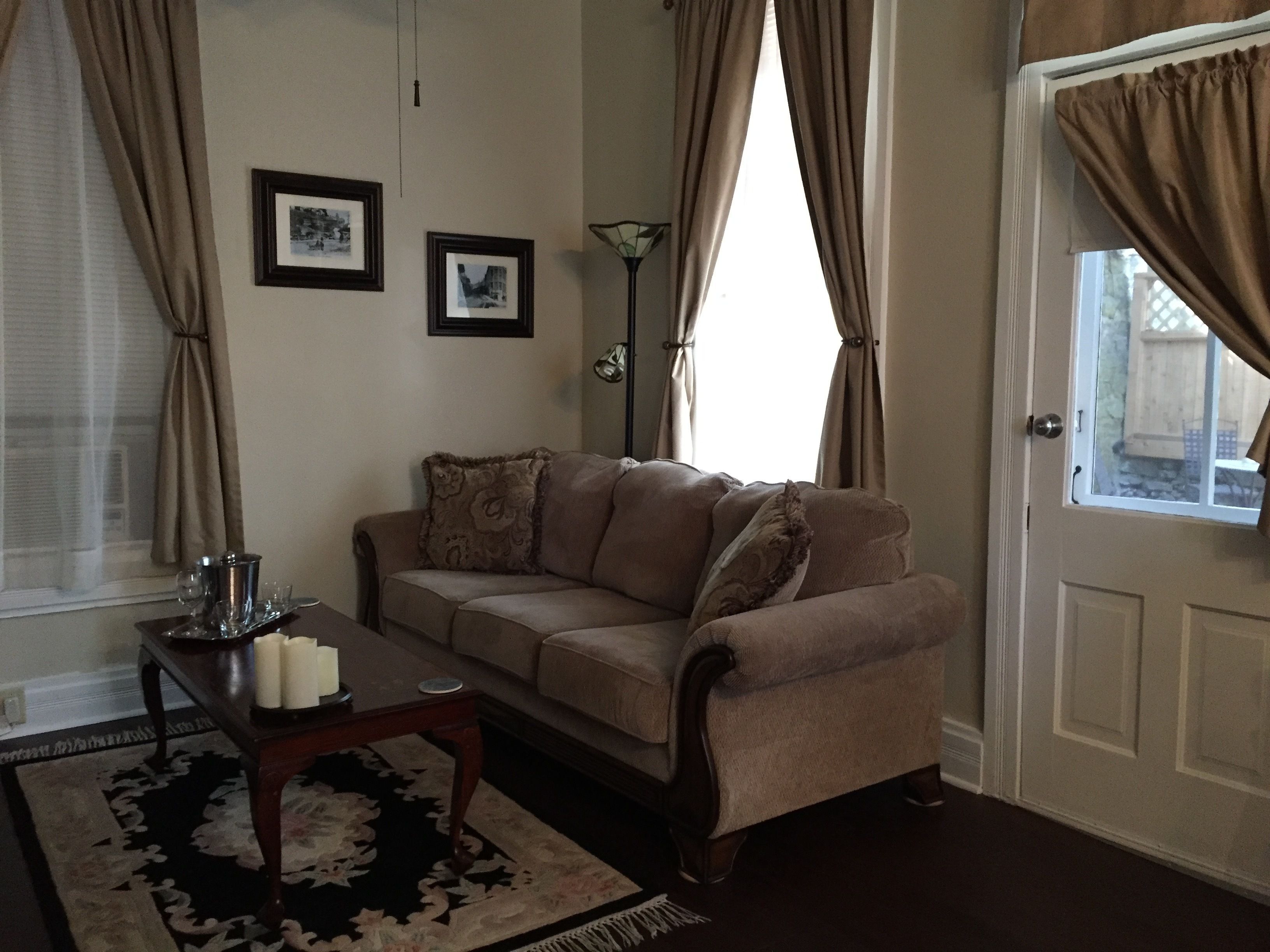 A living room with a beige sofa, a coffee table with candles, framed pictures on the wall, and a window with curtains.