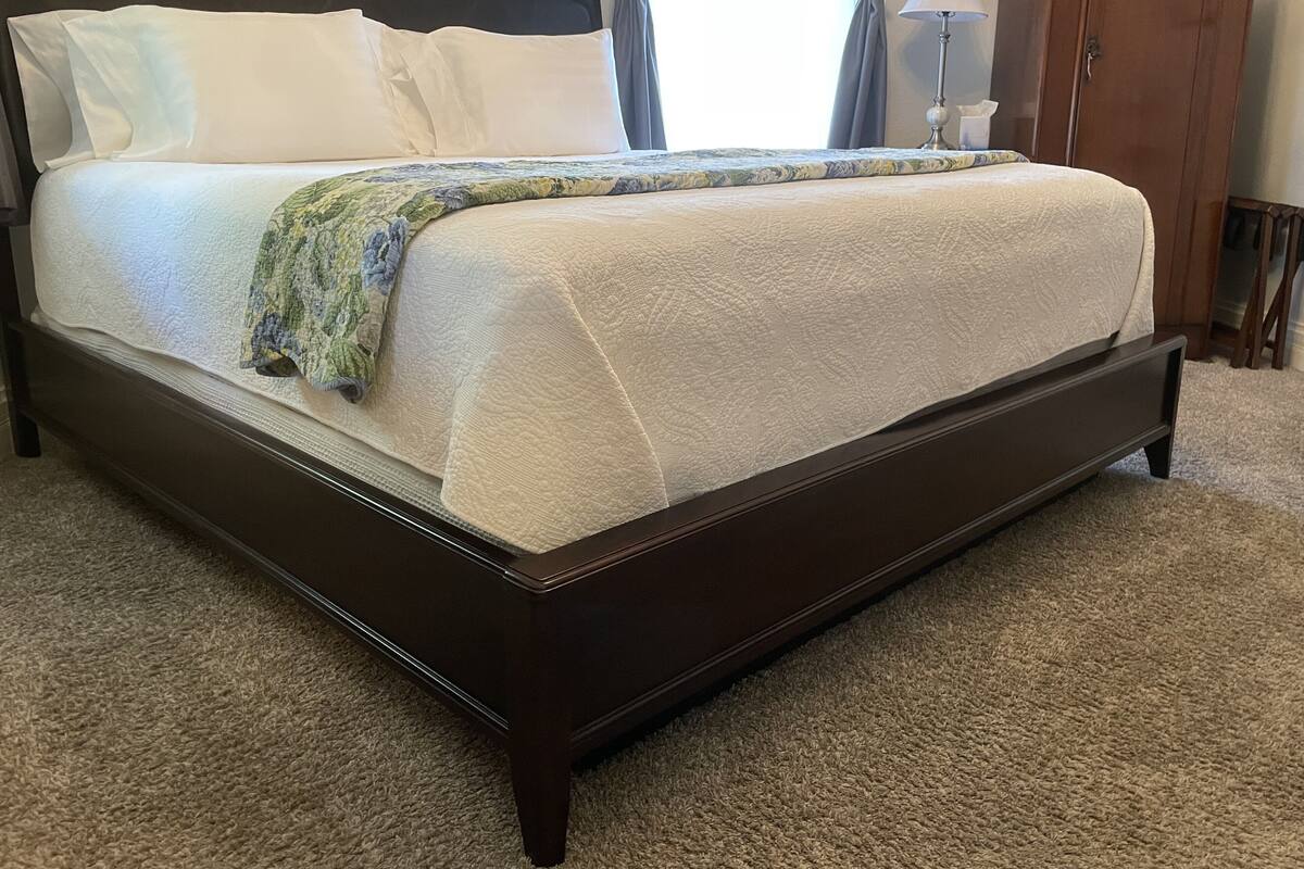 A double bed with a dark wooden frame, white bedding, and a floral throw blanket.