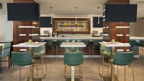 Un espace bar moderne doté d’un long comptoir, de nombreux tabourets et d’une grande variété de bouteilles.
