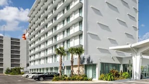 Un hôtel moderne à la façade blanche, doté de nombreux balcons et d’un parking où sont garées des voitures.