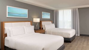 Une chambre d’hôtel avec deux lits, une table de chevet, une lampe et deux tableaux au mur.