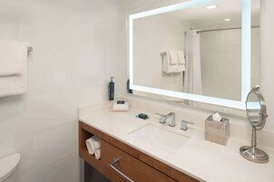 A modern bathroom with a large mirror, white sink, and a wooden vanity.