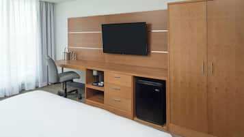 A hotel room with a bed, a desk with a television, a refrigerator, and a wardrobe.