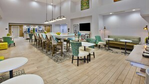A spacious hotel lobby with a dining area, seating arrangements, and a television. - Hampton Inn & Suites Alliance (Alliance)